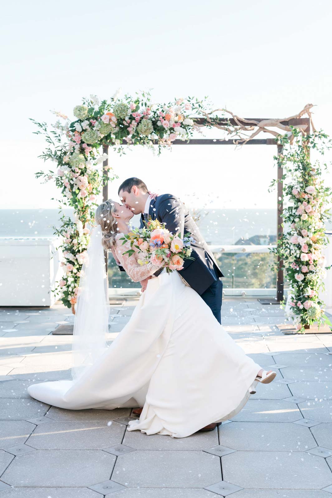 bride and groom kiss and dip while recessing down wedding ceremony aisle while flowers are thrown at them