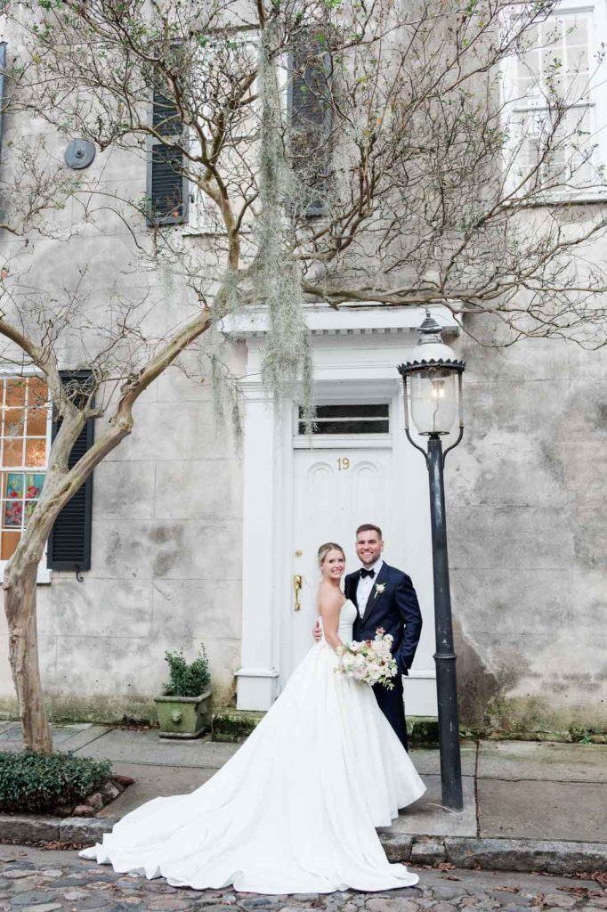bride and groom standing in front of white doorway on cobblestone street