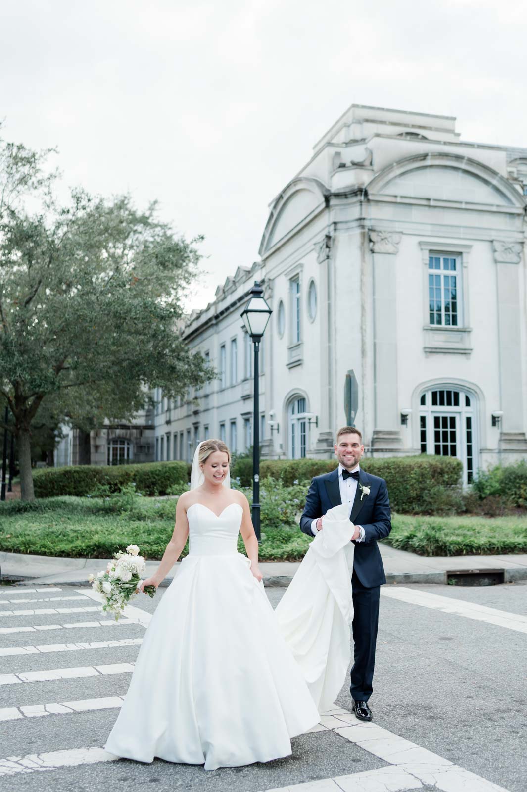 bride crosses street at crosswalk while groom holds her wedding dress