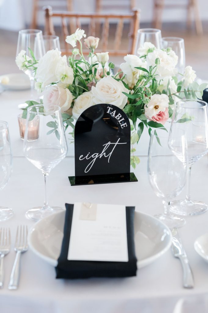place setting at wedding reception table with black table number plaque and white floral bouquet