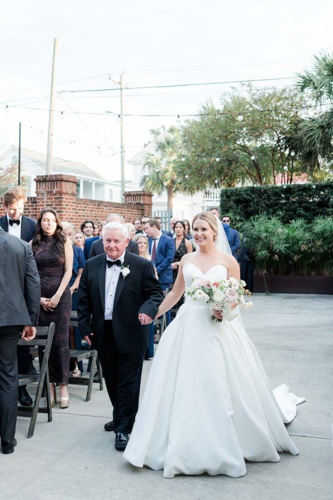 bride processing down the ceremony aisle with her father while guests look on