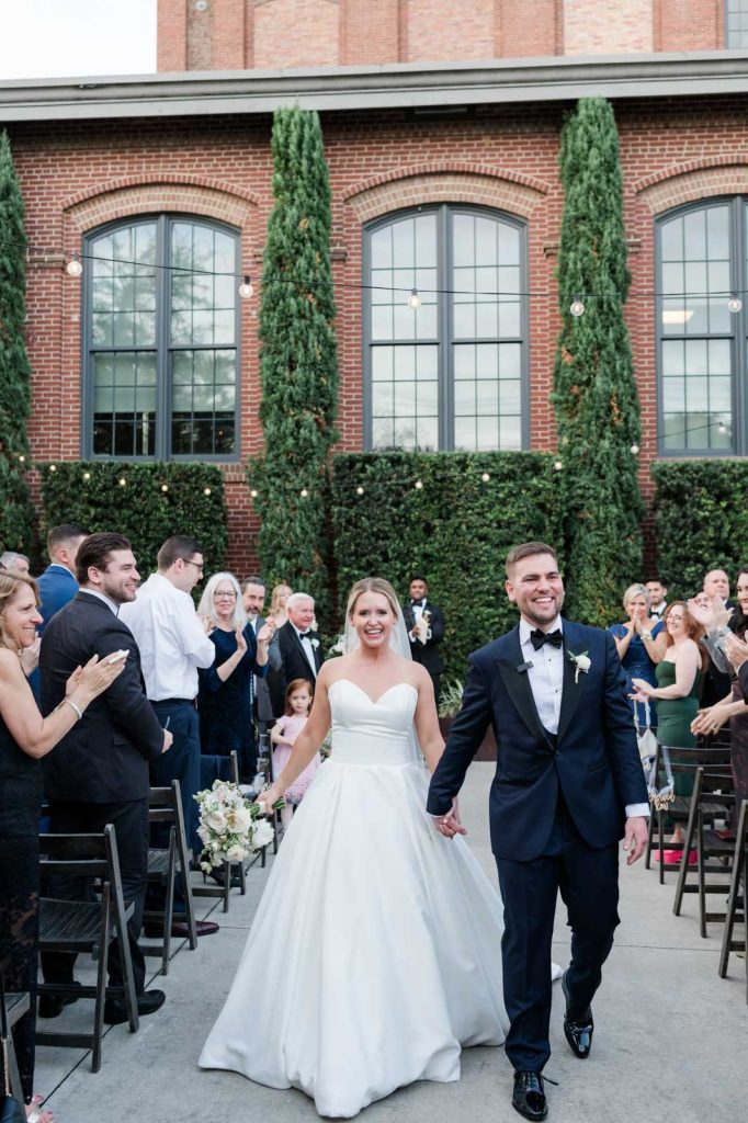 bride and groom holding hands processing down wedding ceremony aisle outside