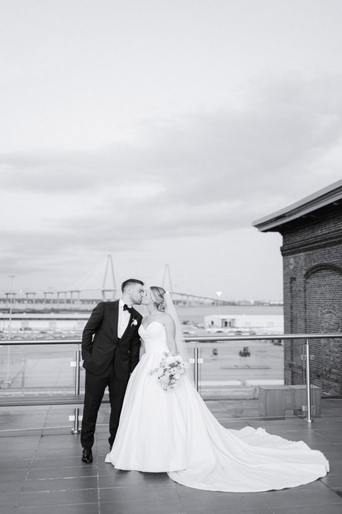 newlywed couple kiss on roof top overlooking Charleston skyline