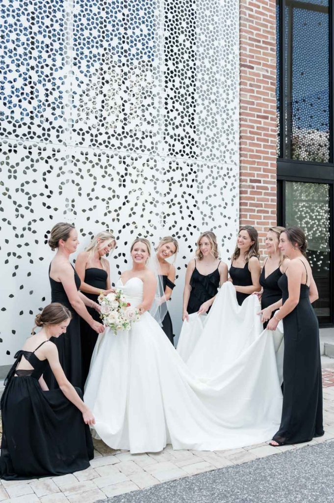 bridesmaids in black dresses holding bride's dress