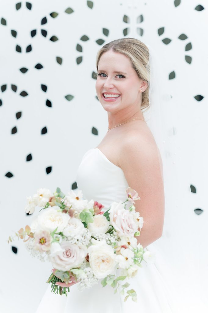 3/4 bridal portrait of blonde bride holding pastel floral bouquet against white backdrop