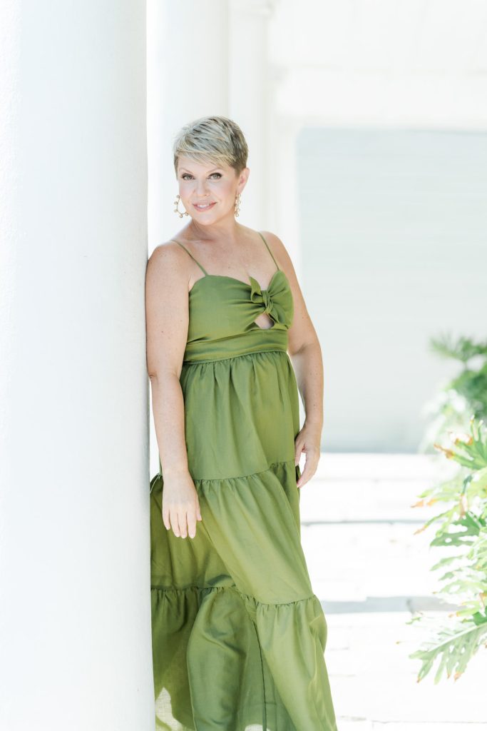 Leigh Hayward leaning against white column wearing long green dress