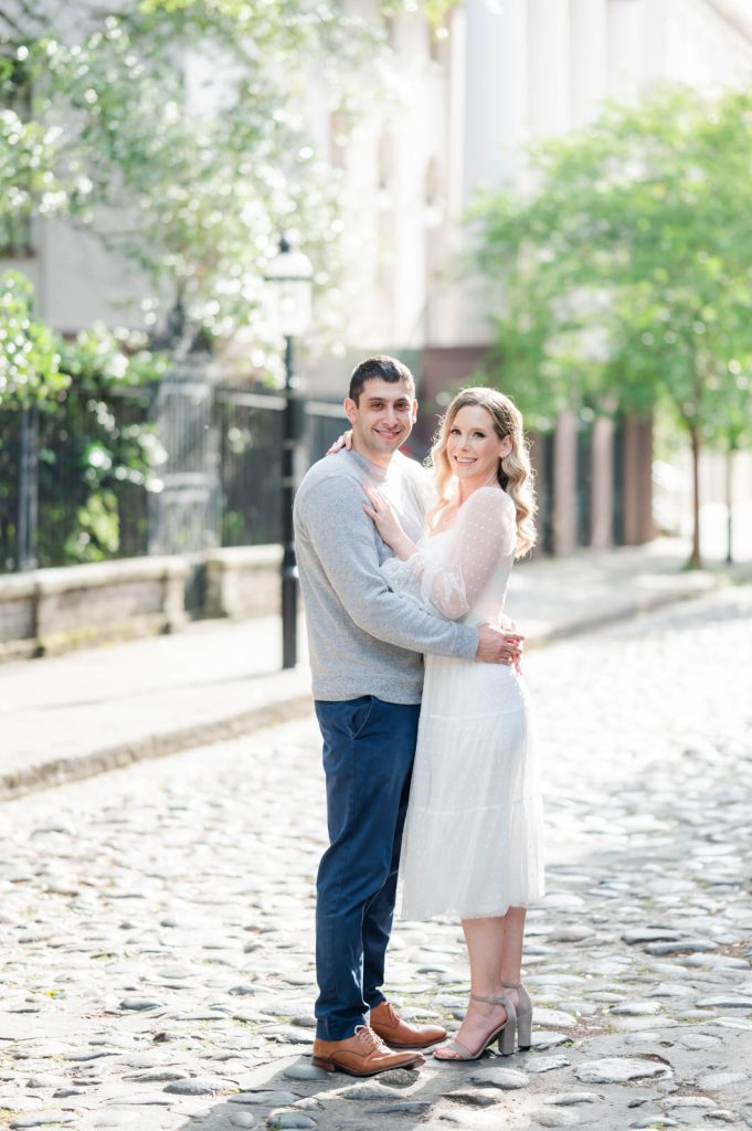 engaged couple stand belly button to button on cobblestone street