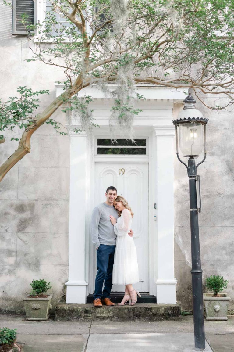 engaged couple stand in door frame, girl leans head on guy's shoulder
