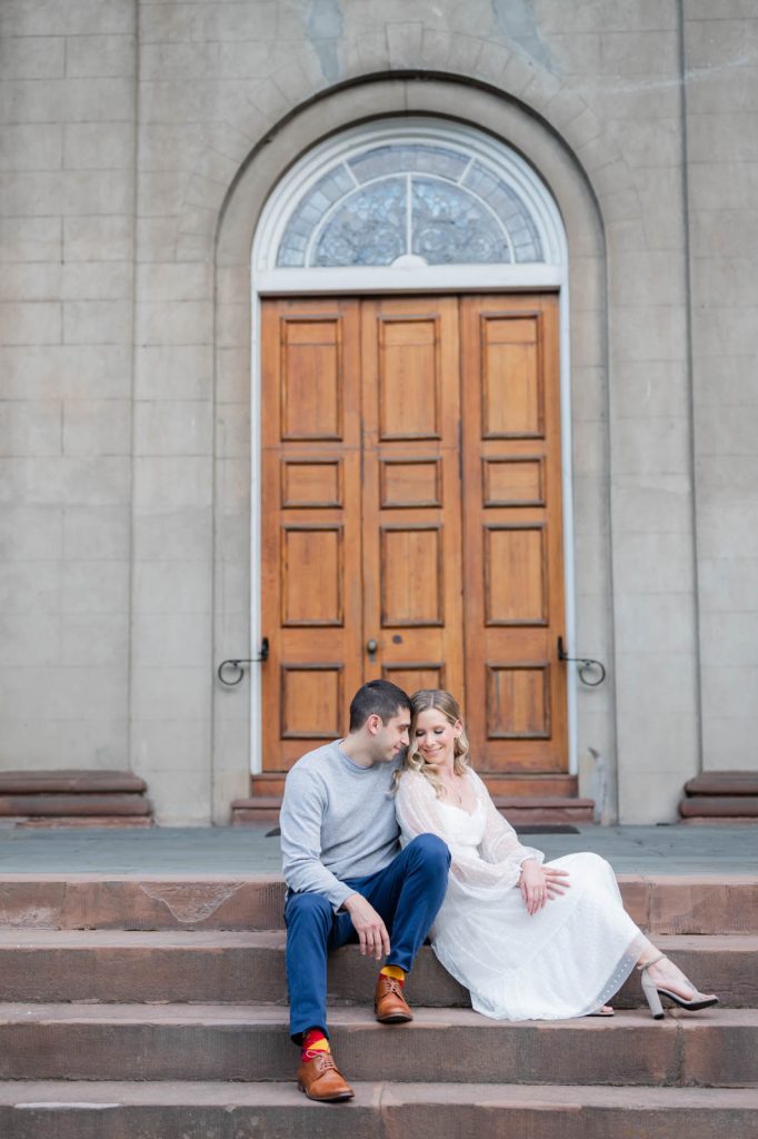 engaged couple snuggle while sitting on church steps
