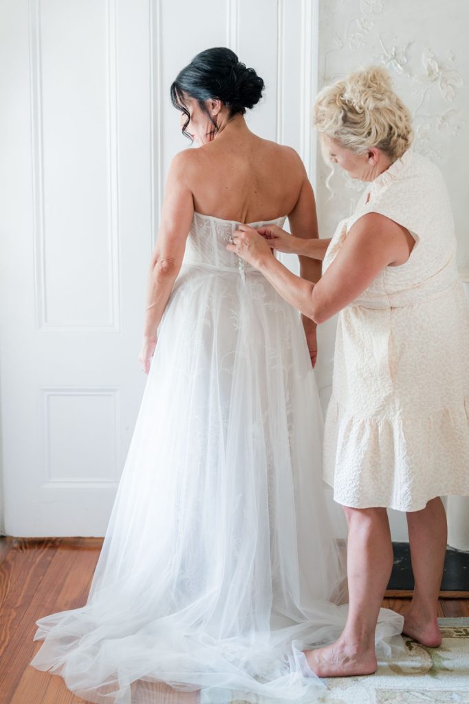 bride getting wedding dress zipped up by friend