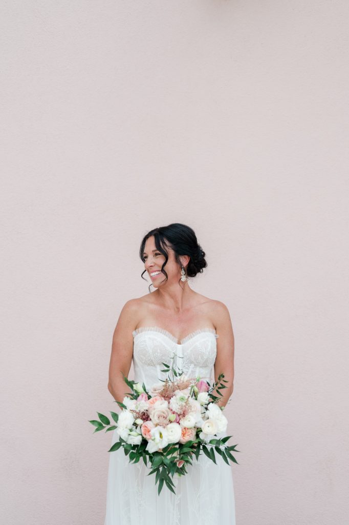 Bride smiles off camera standing against pink exterior wall of Mills House Hotel