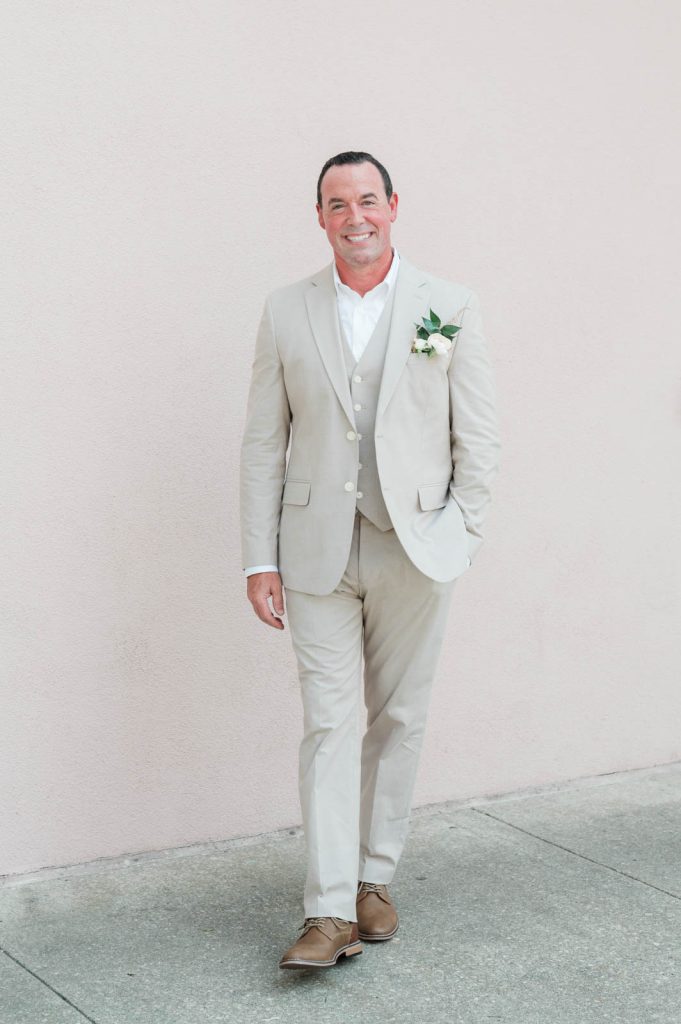 Groom walking away with hand in pocket against pink wall