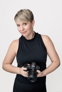 studio portrait of photographer wearing black holding Nikon camera