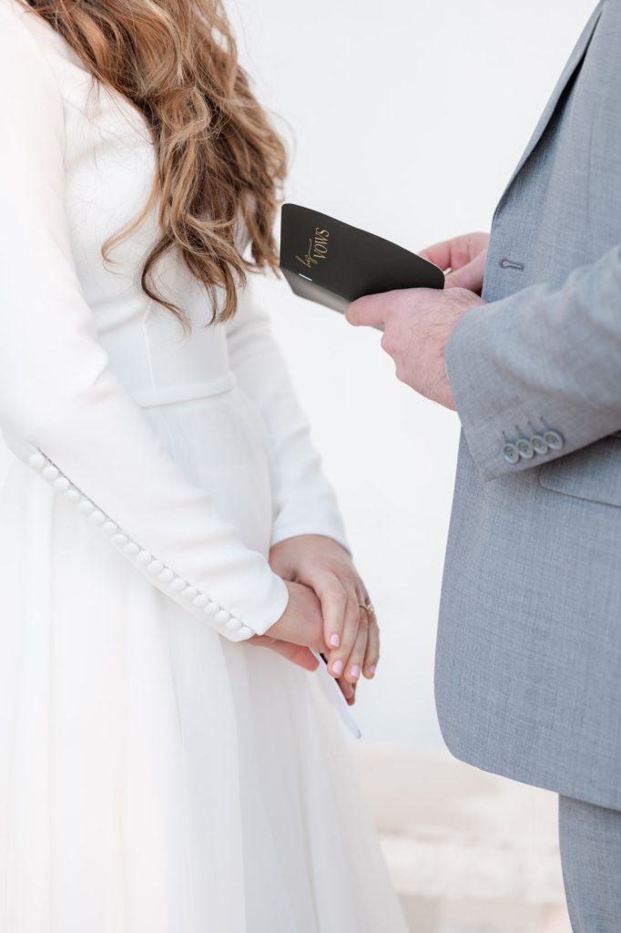 close up of couple's hands while the groom reads his vows from his vow book