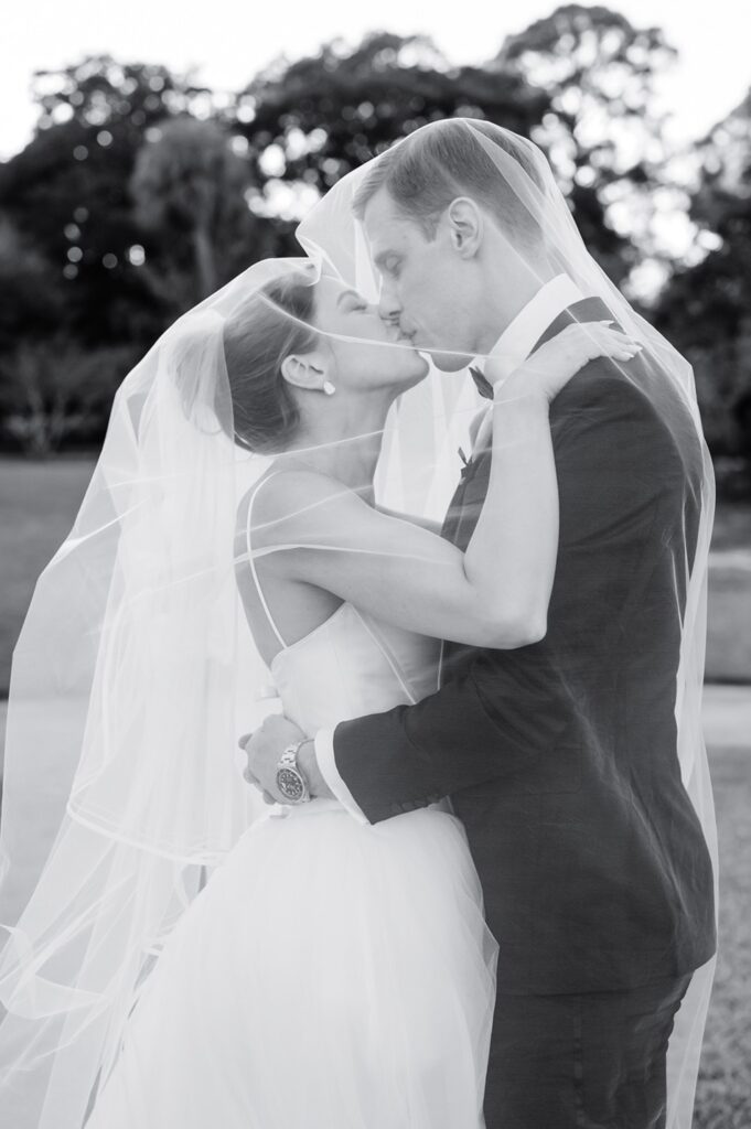 black and white photo of newlyweds while they kiss under bride's veil