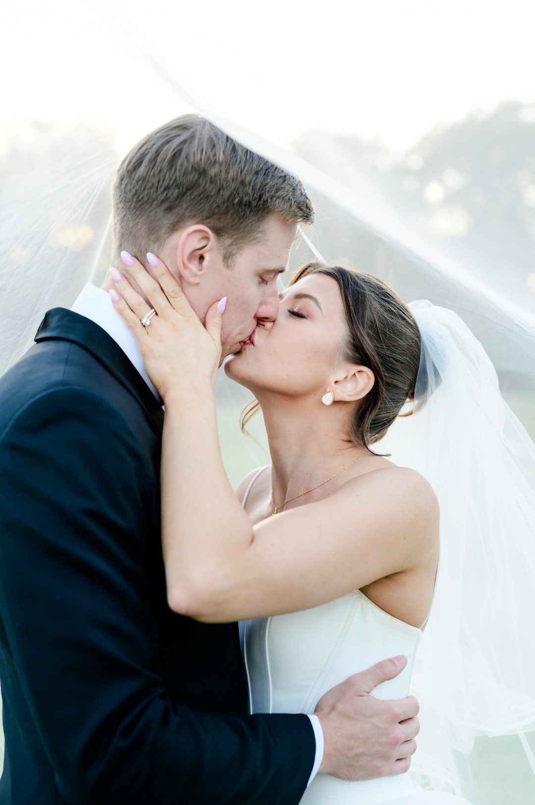 bride grabs groom's cheek pulling him in for a kiss under her veil