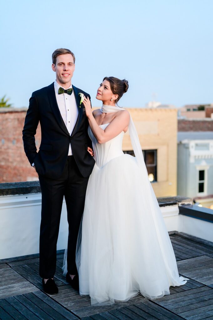 bride holds onto groom' shoulder while standing on rooftop of Surcees