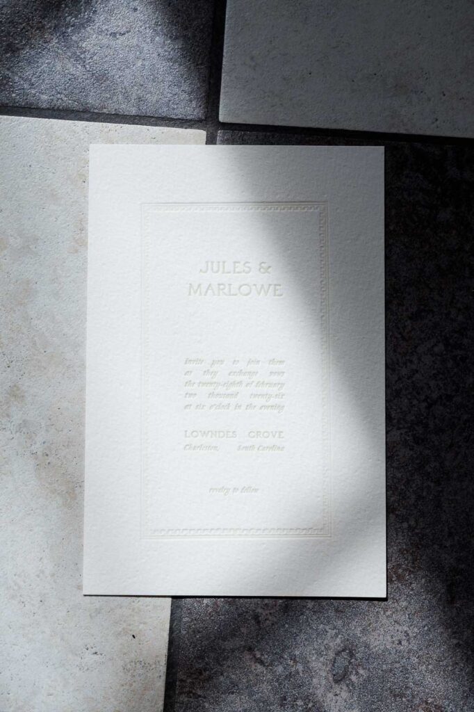 Wedding invitation on black and white checked floor with shadows from light coming in