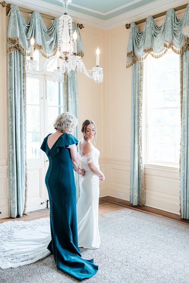 mother zipping up daughter's wedding dress in pink room at Lowndes Grove wedding venue